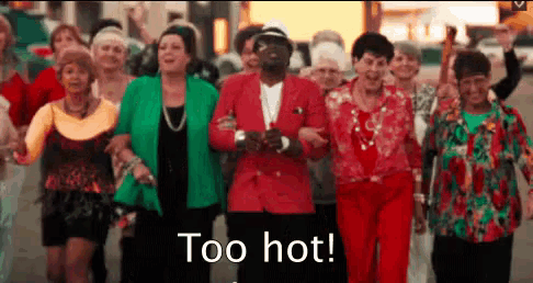 a group of people are walking down a street and a man in a red suit says too hot .