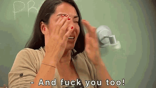 a woman is crying in front of a blackboard and says and fuck you too .