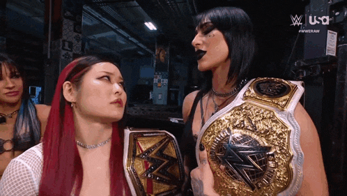 two women holding wrestling championship belts are standing next to each other in front of a screen that says usa