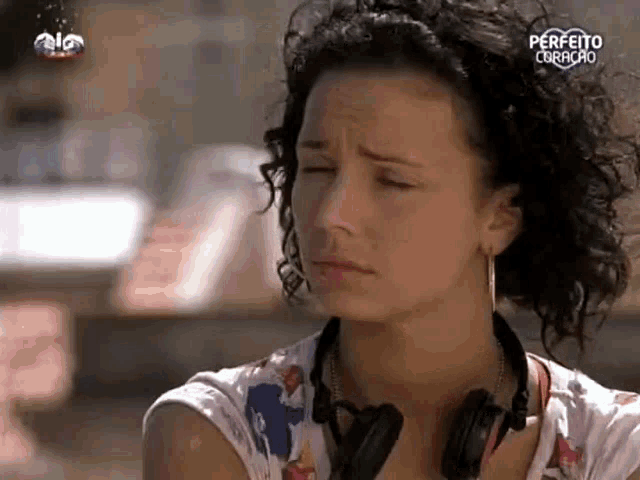 a woman with curly hair wearing headphones and earrings is looking down with her eyes closed .