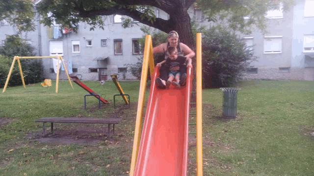 a woman and a child are playing on a red slide in a playground