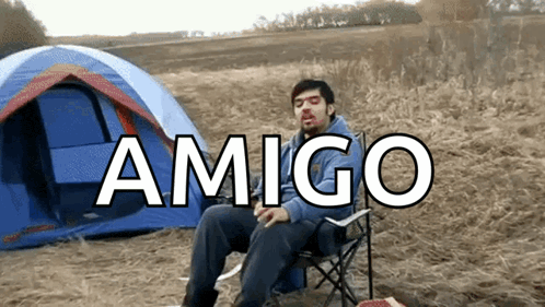 a man sits in a chair in front of a tent with the word amigo written in white
