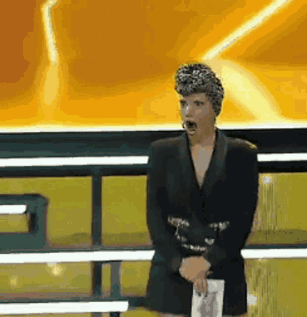 a woman in a black suit is standing on a stage with a microphone .