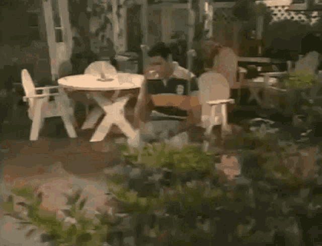 a man is sitting on a patio with a table and chairs in the background .