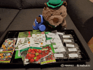 a stuffed animal holding a watering can sits next to a tray full of seeds