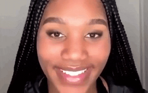 a close up of a woman 's face with braids smiling and looking at the camera .