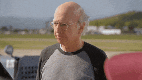 a bald man wearing glasses and a grey shirt looks at something