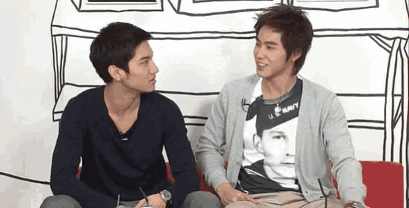 two young men are sitting on a couch and one has a shirt that says u.s. navy