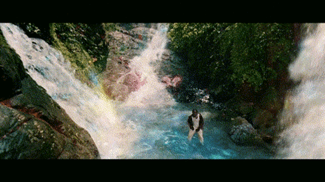 a man is standing in front of a waterfall in the woods