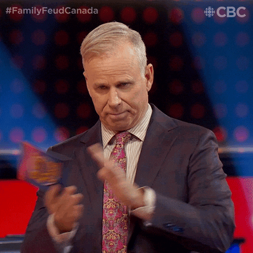 a man in a suit and tie applauds in front of a screen that says family feud canada