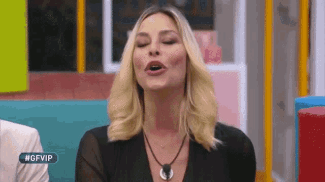 a woman with blonde hair is making a funny face while wearing a black dress and a necklace .