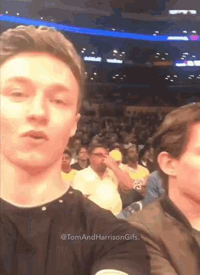 a man taking a selfie in front of a crowd with the words tom and harrison gifs below him
