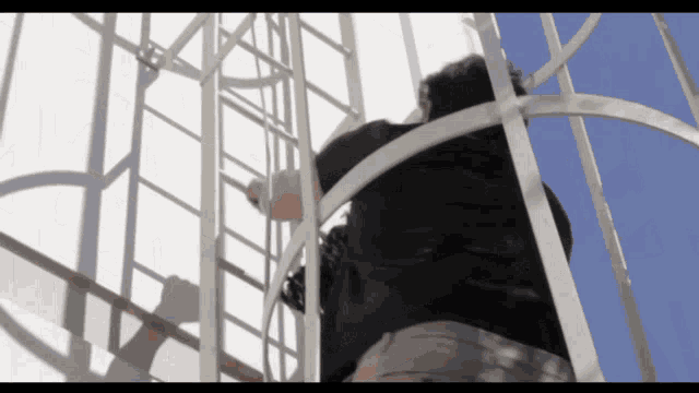 a man climbs up a metal ladder with a blue sky in the background