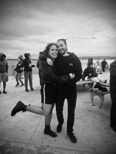 a black and white photo of a man and woman hugging on a pier