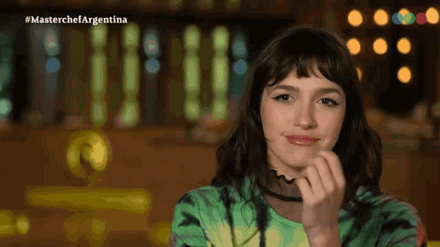 a woman in a green tie dye shirt is smiling in front of a screen that says masterchef argentina
