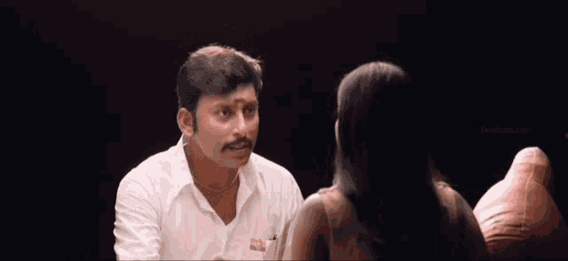 a man in a white shirt has a ball on his head while talking to a woman