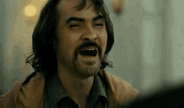 a man with a beard is laughing with his mouth wide open .