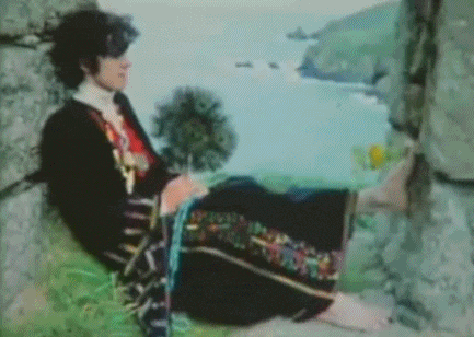 a person in a colorful dress is sitting on a rock near the water