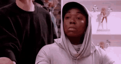 a woman wearing a hooded sweatshirt and a hat is standing in front of a man .