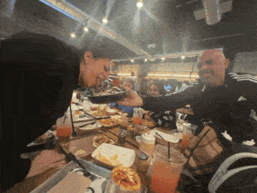 a group of people are sitting at a table eating food and drinking
