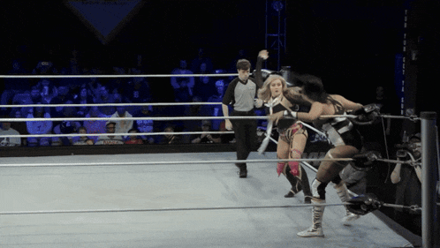 a referee watches two women wrestle in a ring