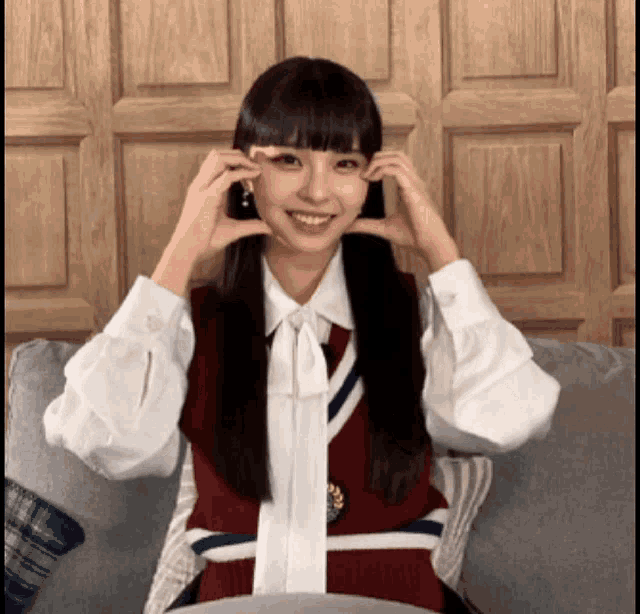 a girl with pigtails is sitting on a couch making a heart shape with her hands