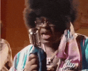 a man with an afro is singing into a microphone while wearing sunglasses .
