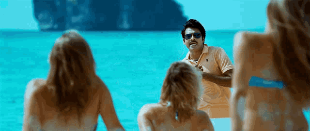a man wearing sunglasses and a polo shirt stands in front of a group of women