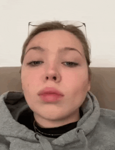 a young woman wearing glasses and a hoodie is sitting on a couch .