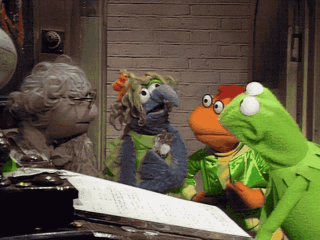a group of stuffed animals including kermit the frog are standing around a table