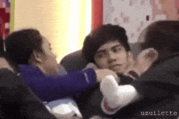 a group of people are sitting in a room and a woman is putting her hand on a man 's neck .