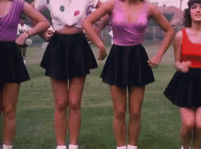 a group of women in short skirts are standing in a field .
