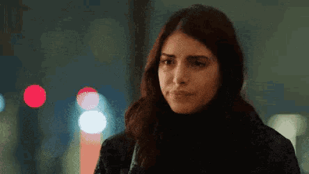 a woman in a black jacket is standing in front of a blurry background .