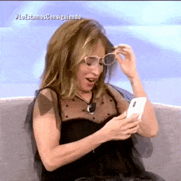a woman sitting on a couch looking at a cell phone with the hashtag #loestamos consiguiendo on the bottom
