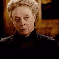 a close up of an older woman wearing a black jacket and earrings looking at the camera .