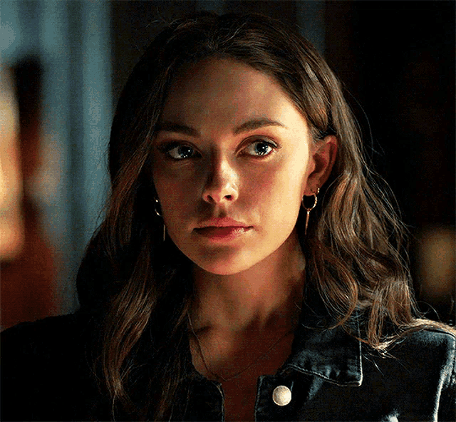 a close up of a woman 's face wearing a black jacket and earrings