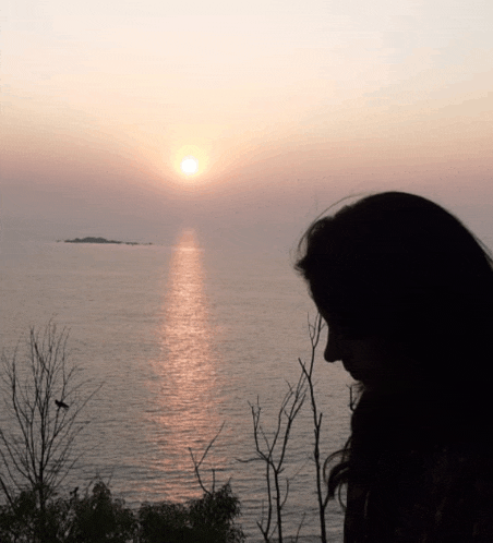 a woman is looking at the ocean at sunset