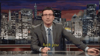 a man in a suit and tie is sitting in front of a city skyline and says " fuck you "