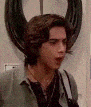 a young man wearing headphones is standing in front of a mirror and making a funny face .