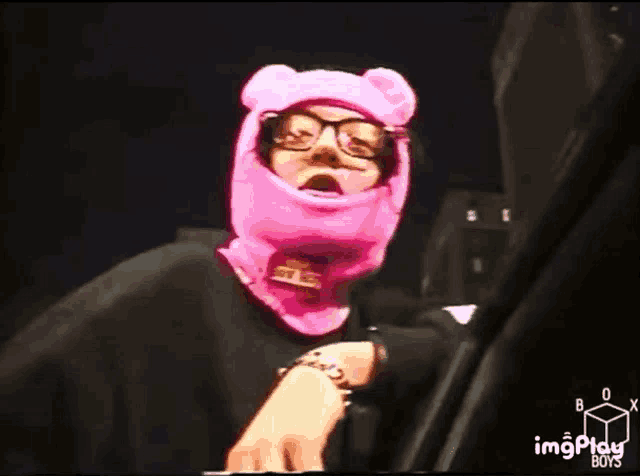 a person wearing a pink bear hat and glasses is standing in front of a keyboard .