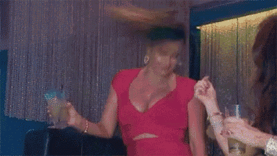 a woman in a pink dress is holding a drink in her hand and giving the middle finger .