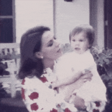 a woman in a floral shirt is holding a baby in her arms