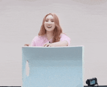 a woman in a pink sweater is sitting on a blue box