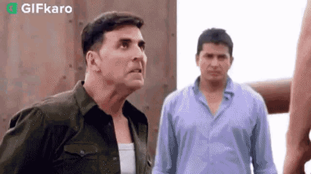 two men are standing next to each other and one of them is looking up at the sky .
