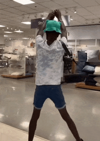 a young man wearing a green hat and shorts is dancing in a store .