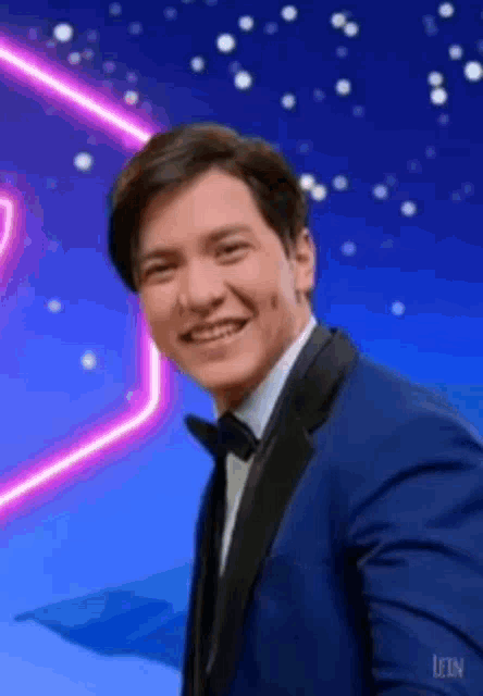 a man in a blue tuxedo and bow tie is smiling .