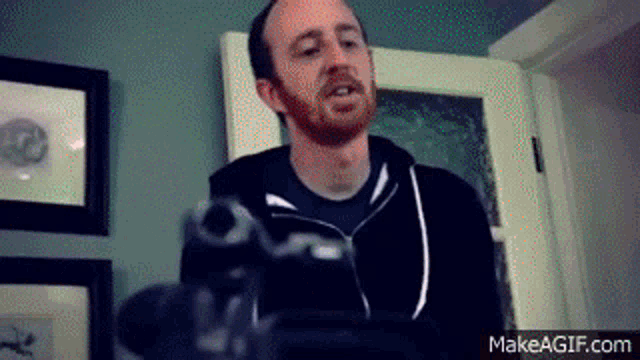 a man with a beard is pointing a gun at the camera and says makeagif.com