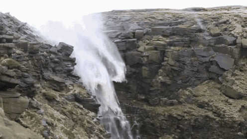 a waterfall is surrounded by rocks and grass on a hillside
