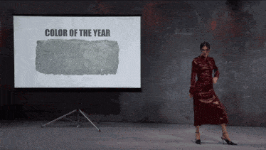 a woman in a red dress is dancing in front of a screen that says color of the year