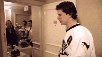 a man in a penguins jersey stands in a room